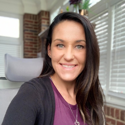 Portrait of a White Lady Smiling at the Camera wearing a purple t-shirt and a black cardigan. Michelle