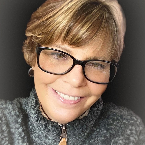 Portrait of a White Lady Smiling at the Camera wearing a grey jumper with a grey backdrop. Tracy