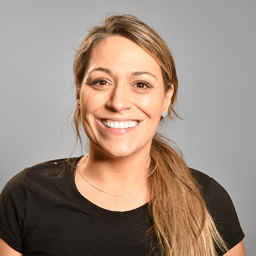 Portrait of a White Lady Smiling at the Camera wearing a dark T-Shirt with a grey backdrop. Jamie