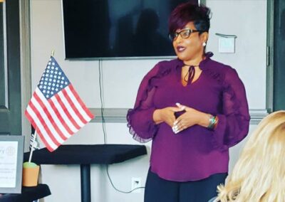 Chanda Giving a Speech in a classroom with an American Flag on the table